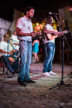 TRINIDAD, CUBA - APRIL 06, 2014: Group of Latino and Afro-American men of musicians play on maracases, guitar and small drums and sing songs on the square in the downtown at nightのeditorial素材