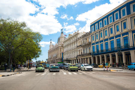 HAVANA, CUBA - APRIL 11, 2016: View to central touristic street of Havana. Colorful bright retro cars, tourists and locals are passing by the alley with tropical palms at summer sunny day. The Capitol behindのeditorial素材