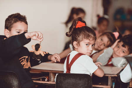 TRINIDAD, CUBA - NOVEMBER 25, 2015: Little girl with serious angry facial expression looks directly. Nearby the boy plays a toy. Children sit at the last school desk at elementary school.のeditorial素材