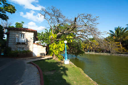VARADERO, CUBA - MARCH 28, 2013: View of the small city river channel on a sunset. Ashore there are a private house and the accurate park with beautiful trees and streetlightのeditorial素材