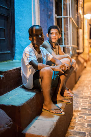 TRINIDAD, CUBA - APRIL 06, 2014: Latin American and Afro-American young boys are smiling and sitting on steps on a porch near the house under a streetlight at night at downtownのeditorial素材