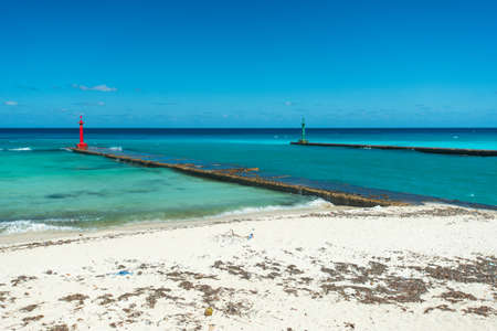 Beautiful view of the sand beach of the azure coastline of the Caribbean Sea in hot sunny summer day. Waves are splashing about a long narrow pier with a red lighthouse at the end. Clear serene blue skyの写真素材