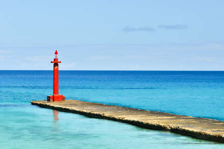 High red color sea lighthouse is on the deserted pier. Beautiful landscape of the coastline of the Caribbean Sea at summer sunny day.の写真素材