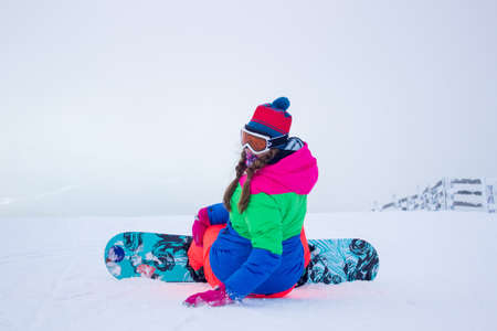 SHEREGESH, RUSSIA - DECEMBER 07, 2016: Sportswoman snowboarder in bright costume and mask prepares for descent from snow top of the mountain on a snowboard downのeditorial素材