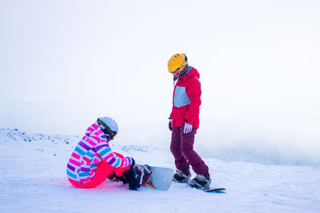 SHEREGESH, RUSSIA - DECEMBER 07, 2016: Two sportsmen snowboarders in bright costume pupil and instructor prepare for descent from snow top of the mountain on a snowboard downのeditorial素材