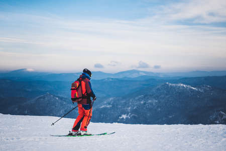 SHEREGESH, RUSSIA - DECEMBER 07, 2016: Man skier in red clothes with backpack goes down from top of snow mountain on skis against the background of snow-covered valley and amazing blue skyのeditorial素材