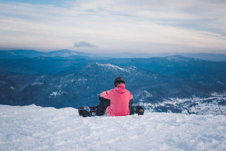 SHEREGESH, RUSSIA - DECEMBER 07, 2016: Sportsman snowboarder in bright costume and mask sits and...