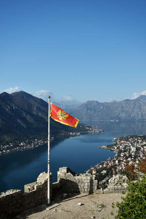 KOTOR, MONTENEGRO Ã¢- NOVEMBER 14, 2014: The flag of Montenegro flutters at top of a stone tower. Sunny day and syrene blue sky. Mountains and river on the background.のeditorial素材