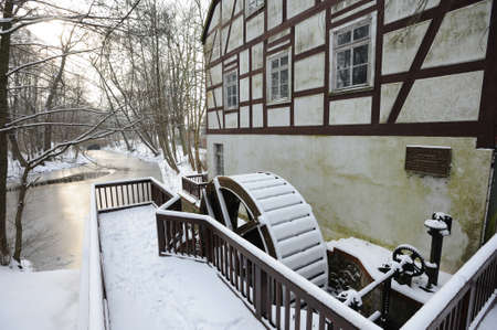 WUSTERHAUSEN, GERMANY - December 11, 2015: A big old wooden waterwheel covered with snow near the waterwheel on a forest and river backgroundのeditorial素材