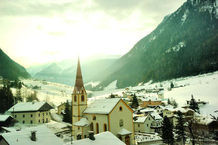 WUSTERHAUSEN, GERMANY - December 11, 2015: View to small city in the mountains. There is a chapel on the background of snow-capped mountains and the bright sun.のeditorial素材