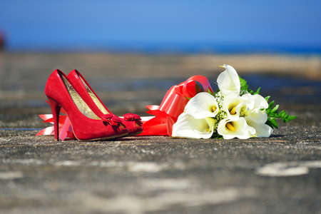 Bridal bouquet and red high-heeled shoes are lying on the pierの写真素材