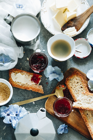 Top view of farm breakfast set with toasts with butter, strawberry jam in jar, flowers and coffeeの写真素材