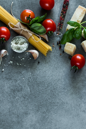 Food frame. Pasta ingredients. Cherry-tomatoes, spaghetti pasta, garlic, basil, parmesan and spices on dark grunge backdrop, copy space, top viewの写真素材