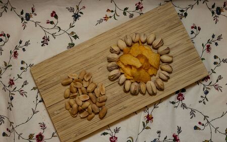 Close up of wooden plate with tasty chips, peanuts and pistachios. Food and beverages concept....