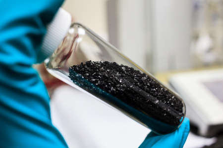 activated carbon charcoal coconut in clear bottom for use in laboratory, holding by green medical rubber hand glove.の写真素材