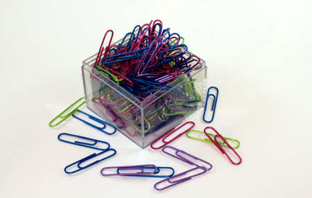 Brightly colored paperclips spilling out of a square, clear acrylic holder.