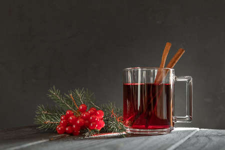 Mulled wine with cinnamon sticks in a transparent glass mug, fir branch and red viburnum berries on a dark backgroundの写真素材