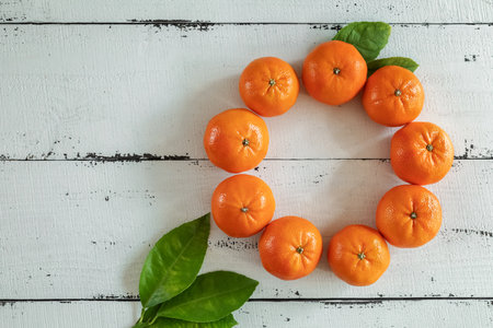 Tangerines with leaves in the form of a Christmas wreath on a background of white wooden boards. The view from the top. Christmas cards and decorations.の写真素材