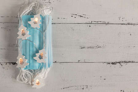 a glowing garland and a stack of medical masks on a white wooden background. concept Christmas and...