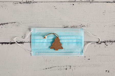 figure of a Christmas tree and a medical mask on a white wooden background. concept Christmas and new year holidays during the coronavirus pandemic with copy space.の写真素材