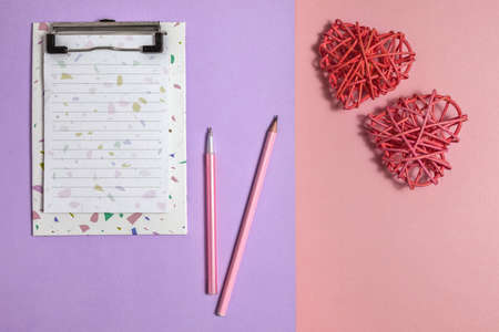 Happy Valentine's Day, February 14.a notebook with a pen and pencil for writing a greeting text and two rattan hearts-symbols of love. on a pink and lilac paper background.の写真素材