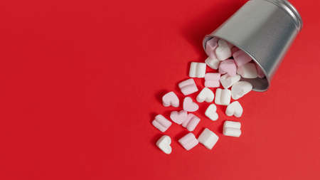 sweets-pink and white marshmallows in the shape of hearts fell out of a tin bucket on a red background. congratulations on Valentine's Day. flat lay, copy spaceの写真素材