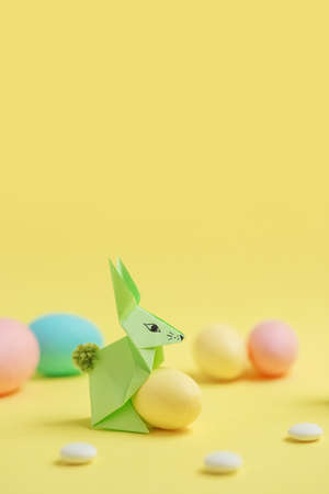 Paper Easter bunny-origami made of colored paper and painted eggs on a delicate yellow background. The concept of the celebration of Easter, greeting card, crafts with your own hands.の写真素材