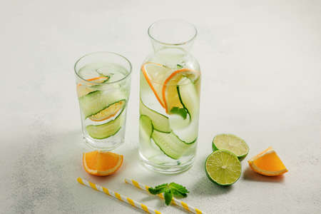 cold homemade lemonade made from cucumber, lemon and mint in a glass bottle and glass, pieces of citrus on a light backgroundの写真素材