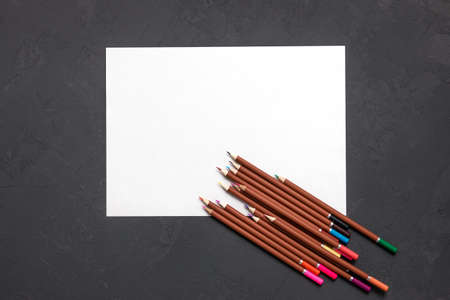 a set of colored pencils and a white sheet of paper on a gray desk. a set for a young artist. the...
