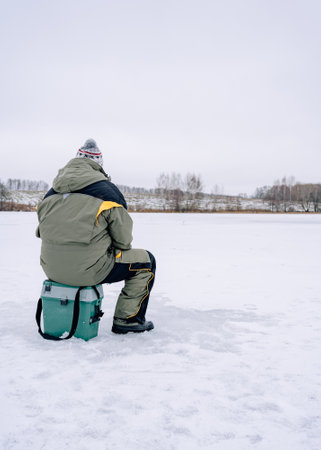 Man Sitting On Box on ice and fishing through holeの写真素材