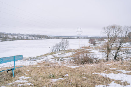 High-voltage tower in field and lake in winterの写真素材
