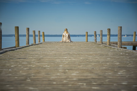 a long pier in a blue lake with a girl sitting atの写真素材