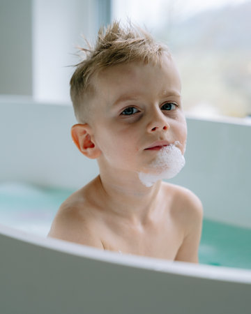 The boy soaks quietly in the modern white bathtub