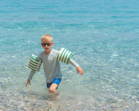 Boy with armbands walking in seaの写真素材