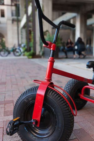 Red tricycle at park with bicycle and chatting women in the backgroundのeditorial素材