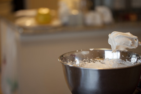 Creamy egg whites/meringue on mixer whisks over bowl with kitchen in backgroundの写真素材