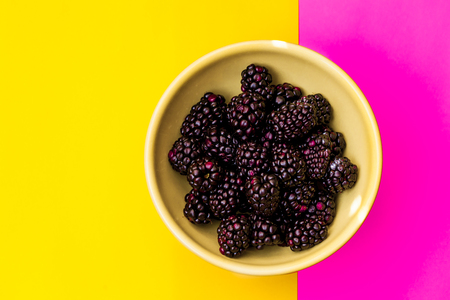 Bowl of blackgerries on color split background, yellow and pinkの写真素材