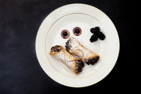 Italian cannoli with chocolate chips on white plate over black backgroundの写真素材