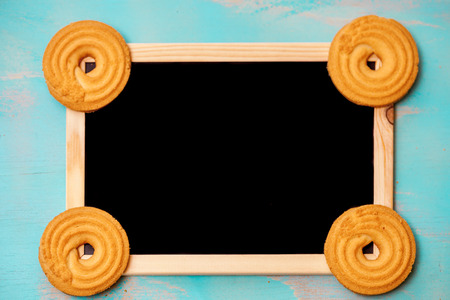 Flat lay design with butter cookies/biscuit and framed blackboard on teal green rustic background,...