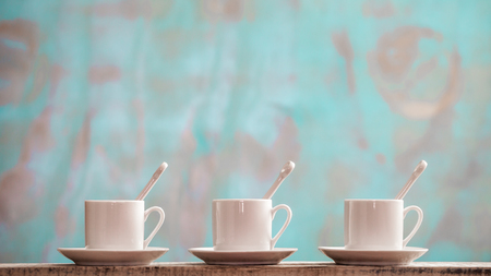 Three small porcelain cups with spoons and saucers against a rustic green background with copy spaceの写真素材