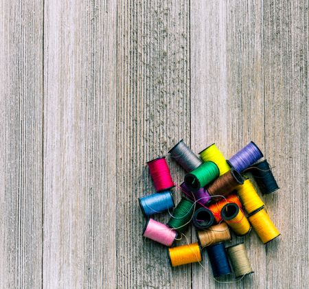 Colorful bobbins with sewing threads piled up on rustic wooden background with copy space