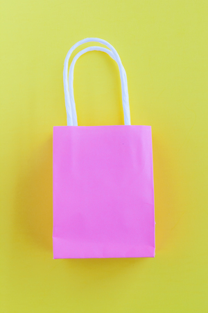 Pink shopping paper bags on bright yellow background with copy space/summer shopping conceptの写真素材