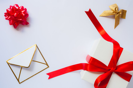 Envelope, golden bow and white gift box with red satin bow and ribbon on white background with copy...