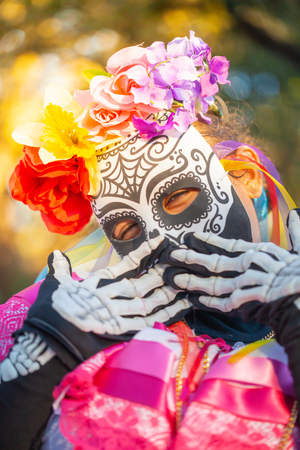 Woman wearing colorful skull mask and paper flowers for Dia de Los Muertos/Day of the Deadの写真素材