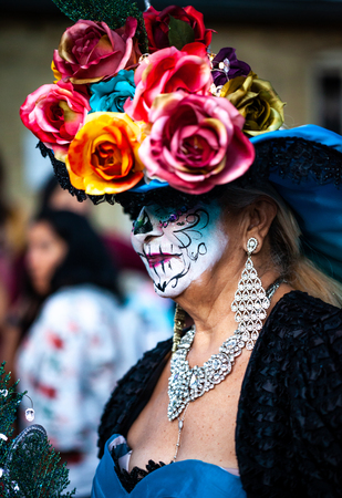 Woman with sugar skull makeup and mexican traditional paper flowers headdress attends dia de los muertos celebrationのeditorial素材