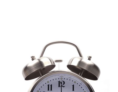 Close up of the top half of an alarm clock with the hand on twelve. The little hammer is blurred...
