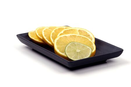 Slices of orange with a slice of lime on a black plate isolated against a white background.の写真素材