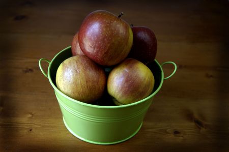 Red apples in a green pail on a country tableの写真素材