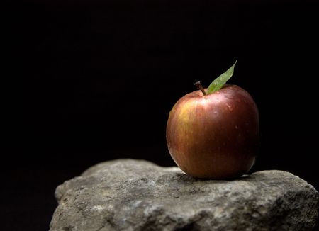 A single red apple balanced on a hard granite stone.