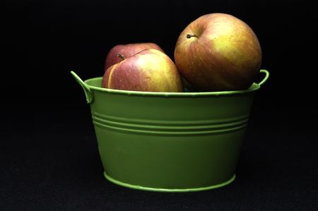 Red apples in a green pail against a black background.の写真素材